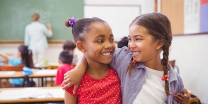 two girls in a classroom with their arms around one another