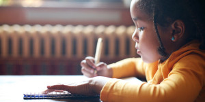 Profile of little African girl writing in classroom.