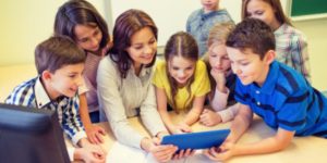 teacher and group of children crowding around a tablet