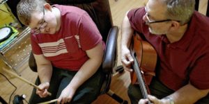 teen with Prader-Willi syndrome drumming with father who plays guitar