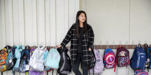 young female asian teacher with row of backpacks